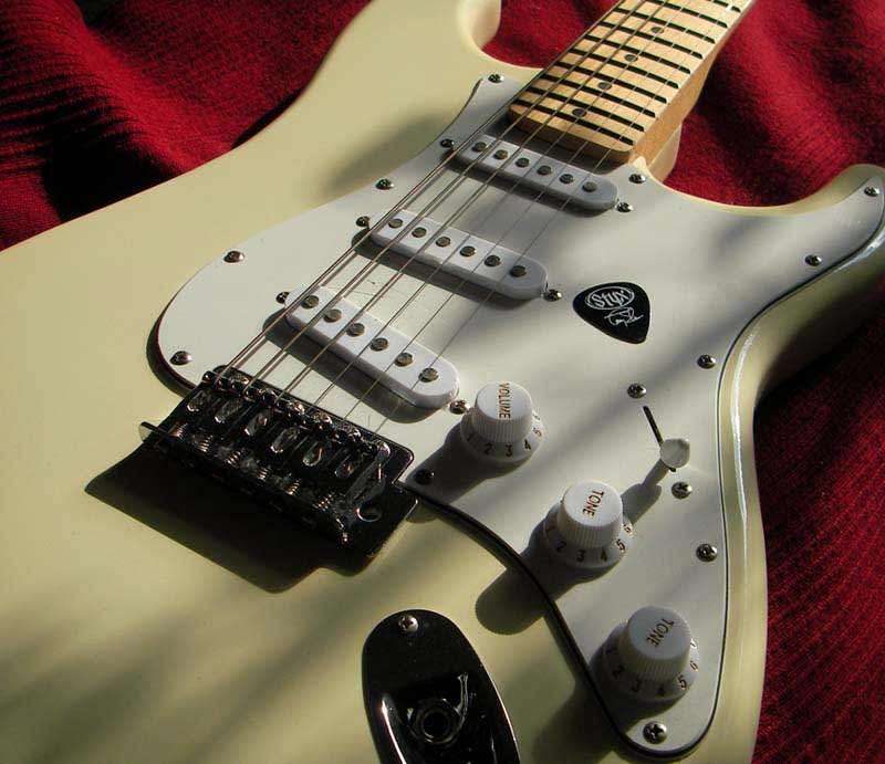 Close up of guitar body in cream with white pick guard.