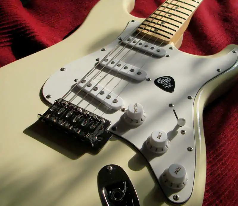 White Fender Stratocaster Body Close-Up Close-up of a white Fender Stratocaster electric guitar featuring a maple neck, white pickguard, controls, and a black Styx guitar pick.